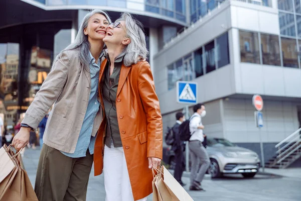 在现代城市街道上，快乐的老年妇女提着购物袋拥抱着一位亚洲女士 — 图库照片
