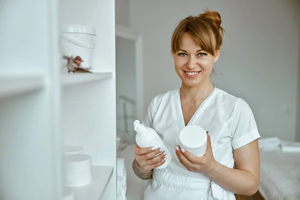 美しい幸せな白人女性マッサージ師は白いミニマルな現代的な治療サロンでポーズをとっています — ストック写真