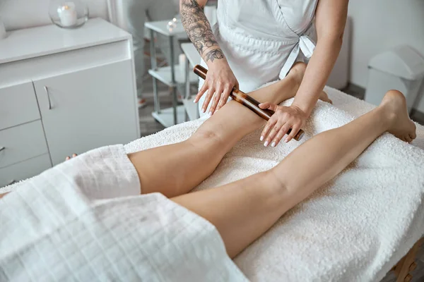 Conident female specialist is doing leg massage with bamboo stick to beautiful caucasean woman client — Stock fotografie