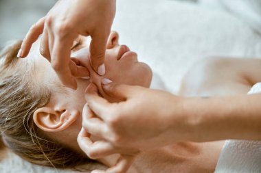 Terapist, modern sağlık dolabında genç bir kadına yüz masajı yapıyor.