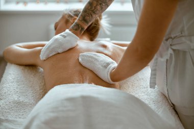 Kendine güvenen kadın uzman, minimalist spa salonundaki güzel beyaz kadın için vücut masajı yapıyor.