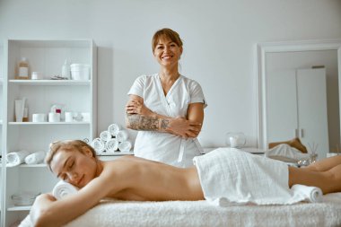 Kendine güvenen kadın uzman, minimalist spa salonundaki güzel beyaz kadın için vücut masajı yapıyor.