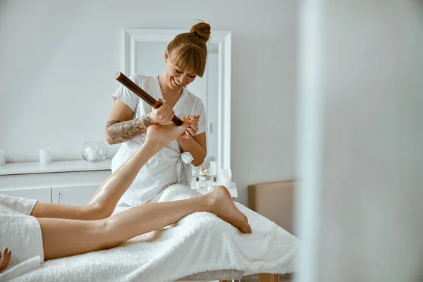 Konsekvent kvinnlig specialist gör ben massage med bambu stick till vackra kaukasiska kvinna klient — Stockfoto