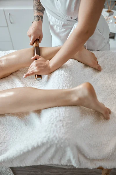 Conident vrouwelijke specialist is het doen van been massage met bamboe vasthouden aan mooie Kaukasische vrouw client — Stockfoto