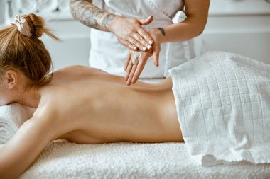 Kendine güvenen kadın uzman, minimalist spa salonundaki güzel beyaz kadın için vücut masajı yapıyor.
