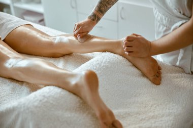Masajcı kadın modern salonda profesyonel bacak masajı yapıyor.