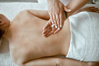 Kendine güvenen kadın uzman, minimalist spa salonundaki güzel beyaz kadın için vücut masajı yapıyor.