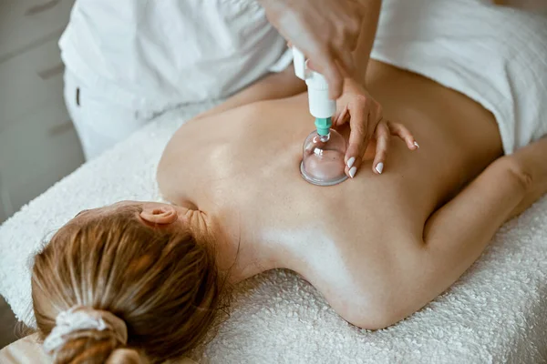 professional female specialist is doing cupping therapy on the back of beautiful caucasian lady