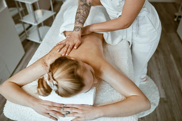 Zelfverzekerde vrouwelijke specialist doet ontspannende lichaamsmassage voor mooie slanke blanke dame bij minimalistische spa salon — Stockfoto