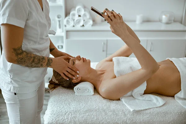 Terapeuta está haciendo masaje facial relajante a una mujer joven en el gabinete de bienestar moderno — Foto de Stock