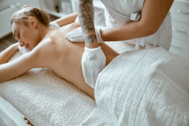 Kendine güvenen kadın uzman, minimalist spa salonundaki güzel beyaz kadın için vücut masajı yapıyor.