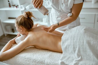 Kendine güvenen kadın uzman, minimalist spa salonundaki güzel beyaz kadın için vücut masajı yapıyor.