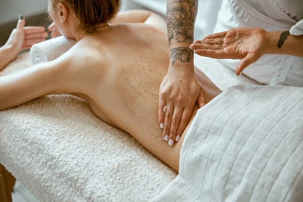 Fiducioso specialista femminile sta facendo massaggio corpo rilassante per bella signora caucasica sottile al salone spa minimalista — Foto Stock