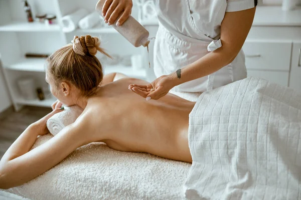 Jistý ženský specialista dělá relaxační masáž pro krásnou štíhlou bělošku v minimalistickém lázeňském salonu — Stock fotografie