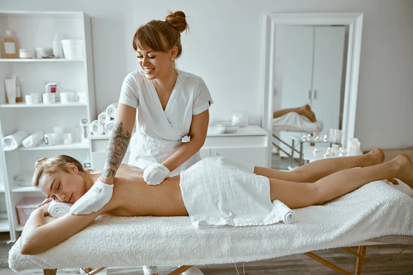 Säker kvinnlig specialist gör avkopplande kroppsmassage för vackra smala kaukasiska dam på minimalistisk spa salong — Stockfoto