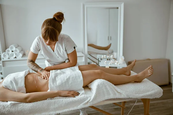 Professionell massage gör magmassage till ung kvinnlig klient i modern wellness salong — Stockfoto