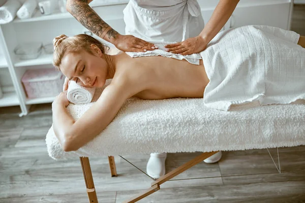 Jistý ženský specialista dělá relaxační masáž pro krásnou štíhlou bělošku v minimalistickém lázeňském salonu — Stock fotografie