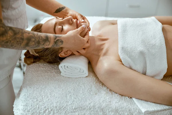Terapeut gör ansikte avkopplande massage till en ung kvinna i moderna wellness skåp — Stockfoto