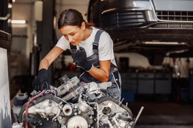 İyi donatılmış bir garajda, çok yetenekli ve yetenekli bir kadın tamirci bir motoru dikkatle inceliyor.