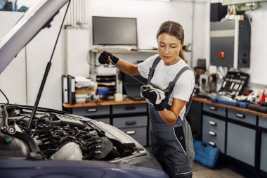 Çok yetenekli ve profesyonel bir kadın tamirci özenle bir garajın içindeki motoru inceliyor.