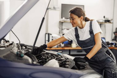 Çok yetenekli bir kadın tamirci profesyonel bir otomotiv atölyesinde motoru dikkatle inceliyor.