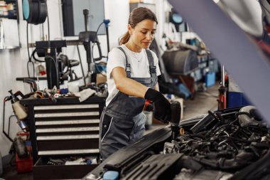 Yetenekli bir kadın tamirci profesyonel bir garajda araba motorunun bakımını ustalıkla yapıyor.
