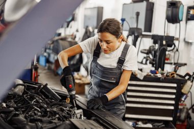 Yetenekli bir kadın tamirci otomotiv tamiri ve teşhis konularındaki uzmanlığını göstermek için bir araba motorunu inceliyor.