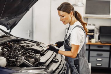 Çok yetenekli bir kadın tamirci profesyonel bir atölyede karmaşık bir araba motorunu ustalıkla inceliyor.