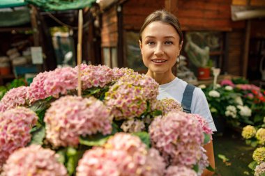 Mutlu bir kadın, yakınlardaki çiçek pazarında canlı ortancalar olan bir resim için sevinçle poz verir.