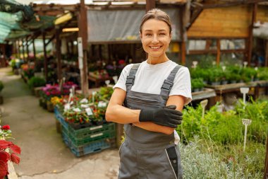Neşeli bir bahçıvan, hayat dolu çiçeklerin ve yemyeşil çiçeklerin arasında mutlu bir poz verir.