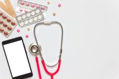 Stetoskop, akıllı telefon ve gri arka planda uyuşturucu. İnternet tıbbı ya da eczane kavramı. Uzayı kopyala, düz olarak.