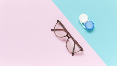 Contact lens case and glasses on blue-purple background. Concept of choice the way vision correction. Flatly, copy space, banner