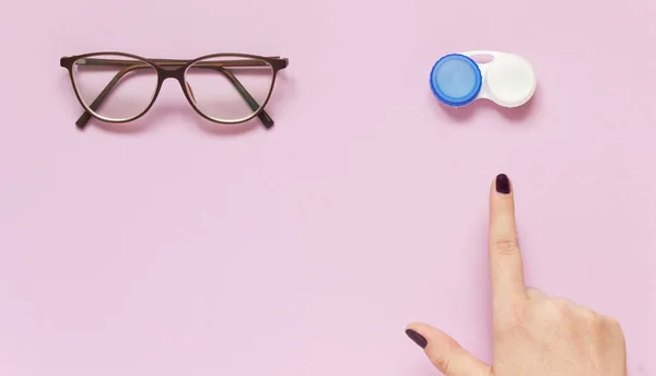 Glasses and contact lens case on purple background. Human hand indicate on lenses. Concept of choice the way vision correction. Flatly, copy space