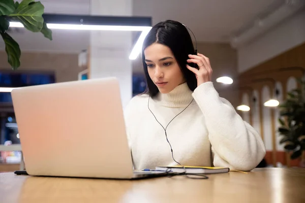 Mulher bonito em fones de ouvido trabalhando digitando no laptop enquanto sentado na mesa no escritório no local de trabalho. Aproveite o processo de e-learning, o uso fácil e conveniente do aplicativo, ouvir música durante o dia útil — Fotografia de Stock