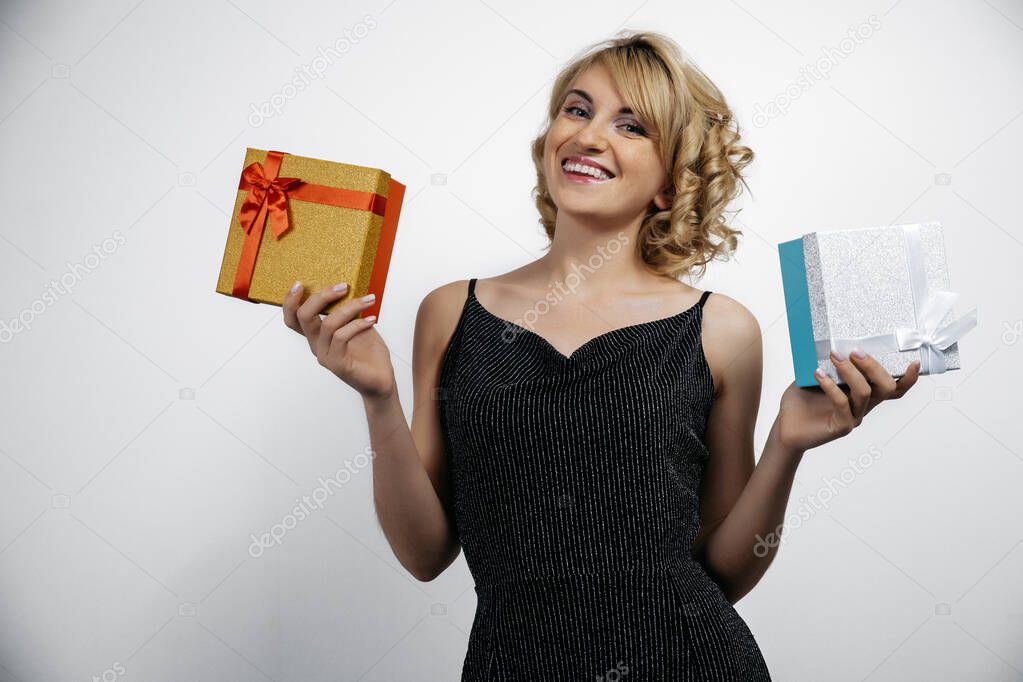 A beautiful girl standing on a white background with gifts in her hands, smiling a beautiful smile. Celebrating Christmas in the office or New year's eve