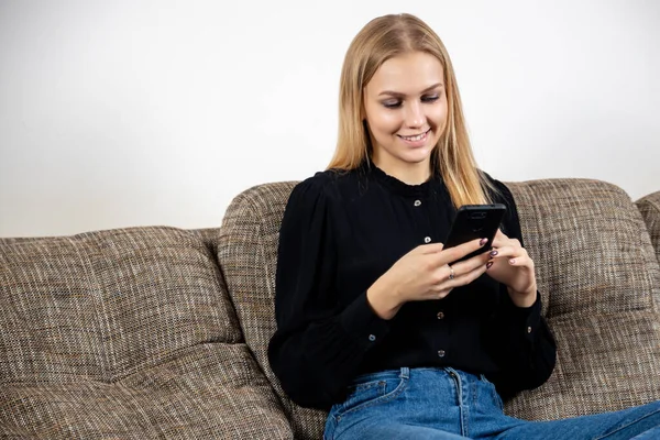 Sorrindo jovem em casa relaxando no sofá, ela está usando um smartphone e texto, tecnologia e conceito de comunicação — Fotografia de Stock