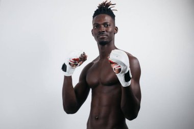 Boks eldivenli kendinden emin bir Afrikalı boksör, gri alanda tek başına dikilirken kameraya uzanıp bakıyor.