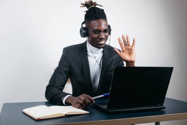 Gülümseyen Afrikalı Amerikalı bir çalışan dizüstü bilgisayar kullanarak, ekrana bakarak, video araması yaparak veya webinar izleyerek, notlar yazarak, uzaktan öğrenme dili konseptiyle, çağrı merkezi operatörüyle çalışarak