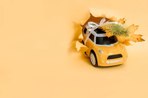 toy car bursts through torn paper, autumn on yellow paper. The concept of a cozy and modern autumn. Trend yellow background, copy space