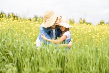outdoor walk. summer in field. yellow flowers, road.Mom hugs her daughter, regrets and protects. upbringing and care. on nature,summer day vacation. playing sunset time. friendly family.