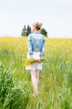 Vertical portrait beautiful blonde girl in a field of daisies. woman in a white dress in a field of yellow flowers. bouquet of daisies. summer village. wildflowers.Goes back, a bouquet behind.