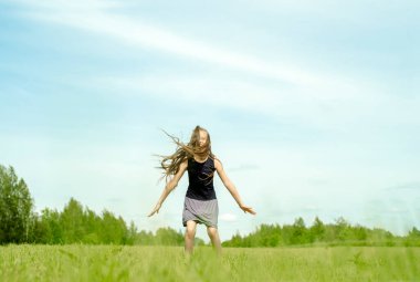 Baharda yeşil çimlerde zıplayan kız çocuğu. Saha, ufuk ve gökyüzü. Mutlu çocukluk ve özgürlük. Açık havada yaşam tarzı..
