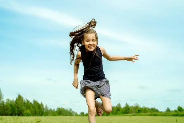 Little girl running on a meadow in a field of flowers, Summer day. barefoot jumping on the grass, happy laughs. Horizon and sky.freshness idea and freedom. happy childhood — Stock Photo, Image