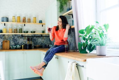 Parlak bir mutfakta genç bir kız bardakta kırmızı kiraz ve elma suyu içer. Modern yaşam tarzı. Sağlıklı yiyecekler, taze meyveler.