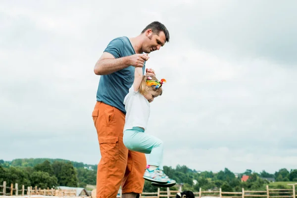 Der Vater spielt mit seinem kleinen Mädchen im Park. Land, Spaziergang ländlicher Straßen.Führt seine kleine Tochter, hält die Hand, aktive Spiele im Freien. — Stockfoto