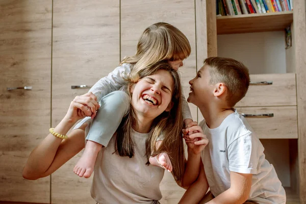 Nasza trójka bawi się w domu i się śmieje. Rodzinne szczęście. radosna gra na podłodze. dwie dziewczyny i brat chłopiec — Zdjęcie stockowe