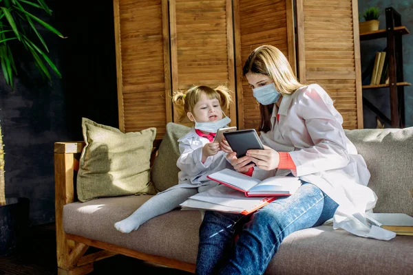 Two cute children play doctor and hospital using stethoscope. girl in uniform of a doctor and in face mask. Coronavirus concept, covid-19.Friends girls having fun at home or preschool.