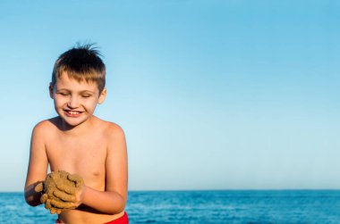 Deniz tatili. Kumsalda kumla oynayan tatlı bir çocuk. Kumdan kale ve pasta kalıpları. Gün batımı, mavi gökyüzü ve rahat seyahat konsepti. Boşluğu kopyala
