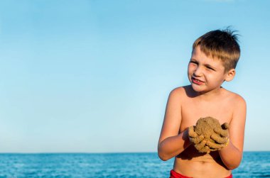 Deniz tatili. Kumsaldaki sevimli çocuk kumla oynuyor. Kumdan kale ve pasta kalıpları. Günbatımı, mavi gökyüzü ve rahatlama seyahat kavramı. Kopyalama alanı