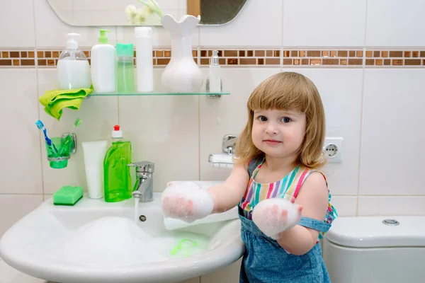 baby girl washing her face, washing her hands and brushing her teeth. morning hygiene. in the white bathroom at home